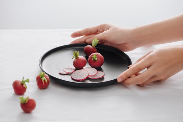 Rábanos rojos frescos con tallo y raíces en un plato negro en la mesa