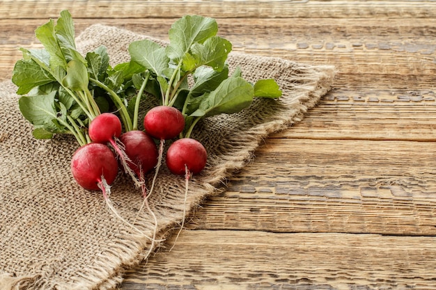 Rábanos rojos maduros con hojas verdes sobre tela de saco y tablas de madera