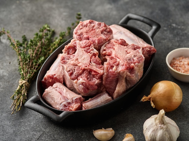 Rabo cru cortado em uma bandeja com especiarias cebola e alho para cozinhá-lo na mesa cinza