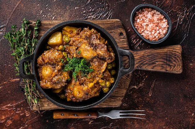 Rabo de boi cozido com vinho e legumes em uma panela. Fundo escuro. Vista do topo.