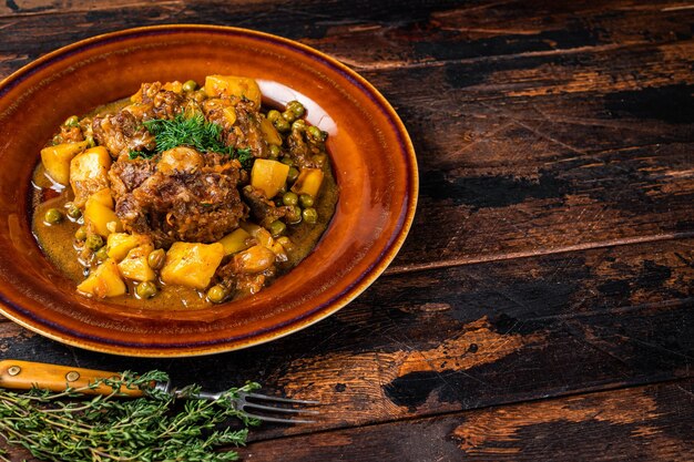 Rabo de boi de vitela com legumes em prato rústico. Fundo de madeira escuro. Vista do topo. Copie o espaço.