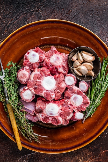 Rabo de toro de ternera cruda fresca carne cortada en placa rústica con hierbas