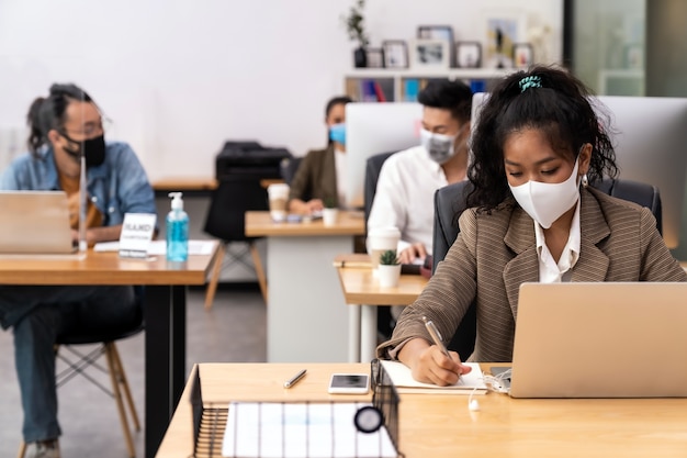 Raça mista de mulher de negócios africana negra e asiática usa máscara facial trabalhando em um novo escritório normal com distância social para Grupo de pessoas da equipe de negócios para prevenir a propagação do coronavírus COVID-19