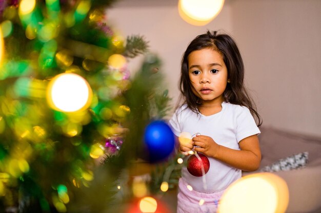 Raça mista linda garota decorando uma árvore de natal na manhã de natal no quarto e desejando um desejo