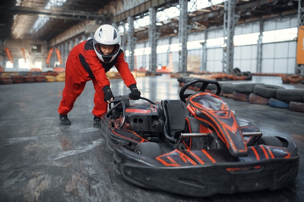 Racer en casco empujando un coche de karts, karting auto sport indoor.