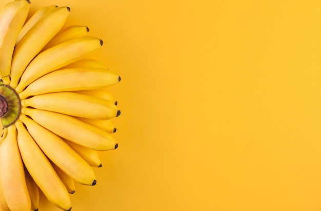 Un racimo de pequeños plátanos maduros sobre un fondo amarillo copia espacio