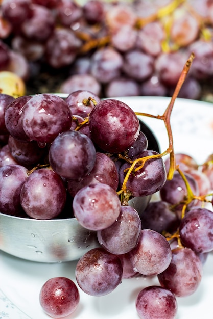 Racimo de uvas oscuras con gotas de agua en un recipiente de metal