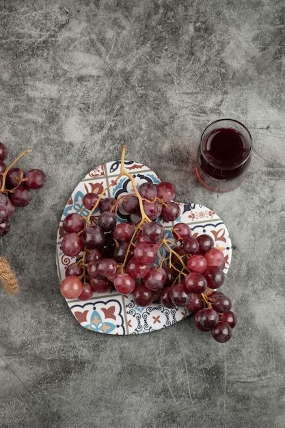 Racimo de uvas rojas frescas y vaso de jugo en la mesa de mármol.