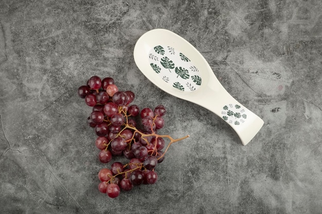 Racimo de uvas rojas y plato blanco vacío sobre superficie de mármol.