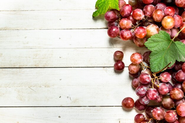 Racimos de uvas rojas con hojas sobre mesa de madera blanca.