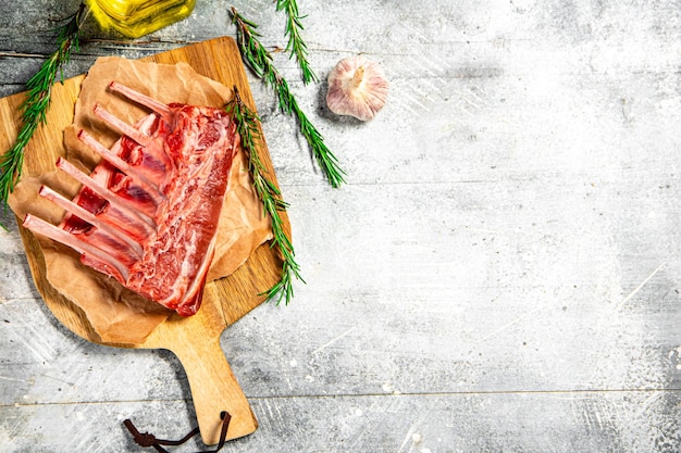 Rack de cordero crudo en una tabla de cortar con aceite y romero