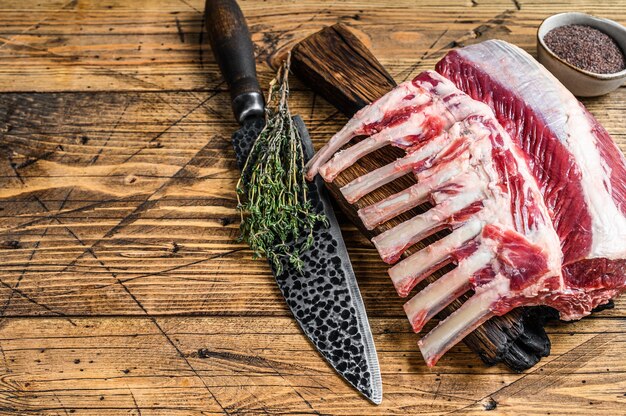 Rack de costillas de cordero crudo sobre una tabla de cortar con un cuchillo. fondo de madera. Vista superior. Copie el espacio.