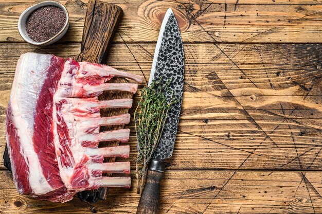 Rack de costillas de cordero crudo sobre una tabla de cortar con cuchillo