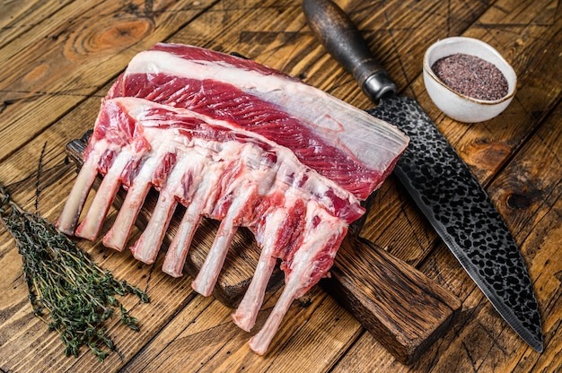 Rack de costillas de cordero crudo sobre una tabla de cortar con cuchillo