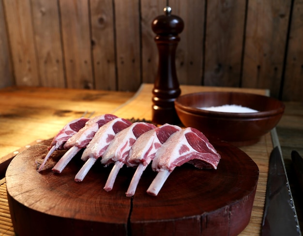 Rack francés Piezas crudas de cordero cortadas en una tabla de madera con sal y pimienta en el fondo