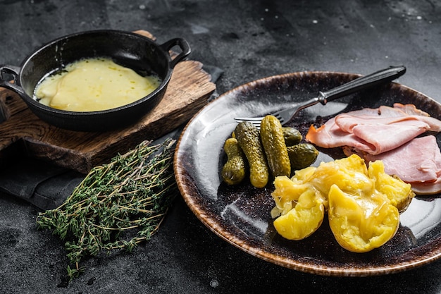 Raclette Queijo derretido com batata cozida e presunto na refeição suíça de prato rústico Fundo preto Vista superior