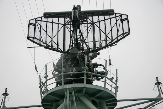 Radar auf einem Kriegsschiff mit einer kreisförmigen Plattform für Menschen. Viele Drähte und Teile. Regnerisches trübes Wetter.