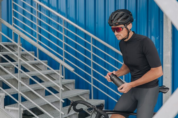 Radfahrer, der auf dem Fahrrad sitzt und eine Flasche Wasser hält