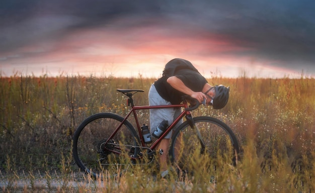 Radfahrer im Feld, der sein Vorderrad überprüft Abenteuer auf dem Fahrrad