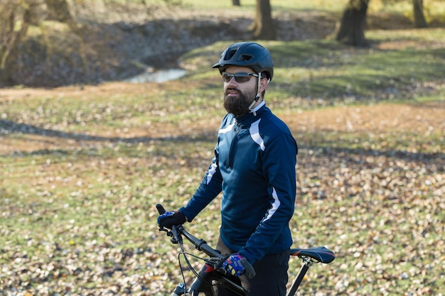 Radfahrer in hose und fleecejacke auf einem modernen carbon-hardtail-bike mit luftfedergabel fährt im gelände der typ ruht sich auf einer bank im herbstpark aus