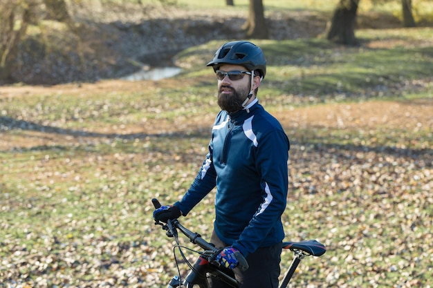 Radfahrer in Hose und Fleecejacke auf einem modernen Carbon-Hardtail-Bike mit Luftfedergabel fährt im Gelände Der Typ ruht sich auf einer Bank im Herbstpark aus