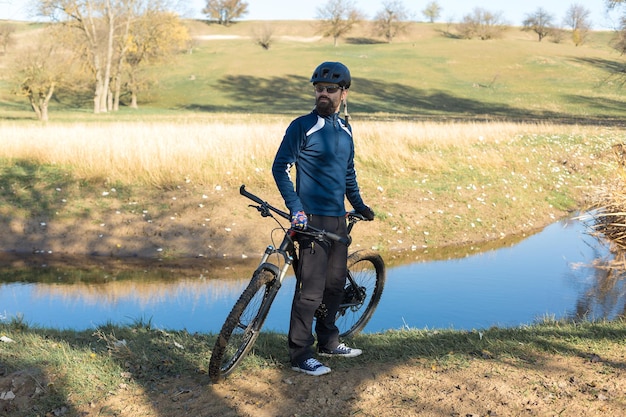 Radfahrer in Hose und Fleecejacke auf einem modernen Carbon-Hardtail-Bike mit Luftfedergabel fährt im Gelände Der Typ ruht sich auf einer Bank im Herbstpark aus