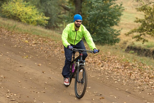 Radfahrer in Hose und grüner Jacke auf einem modernen Carbon-Hardtail-Fahrrad mit Luftfedergabel Der Typ oben auf dem Hügel fährt Fahrrad