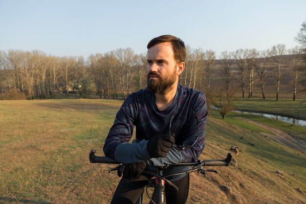 Radfahrer in Shorts und Trikot auf einem Carbonrad mit Luftfedergabel auf einer Klippe stehend