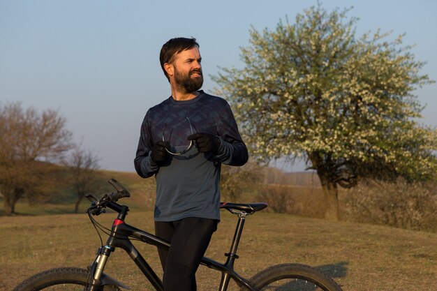 Radfahrer in Shorts und Trikot auf einem Carbonrad mit Luftfedergabel auf einer Klippe stehend