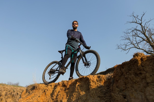 Radfahrer in Shorts und Trikot auf einem modernen Carbon-Hardtail-Bike mit einer Luftfedergabel, die auf einer Klippe vor dem Hintergrund eines frischen grünen Frühlingswaldes steht