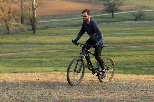 Radfahrer in Shorts und Trikot auf einem modernen Carbon-Hardtail-Bike mit einer Luftfedergabel, die auf einer Klippe vor dem Hintergrund eines frischen grünen Frühlingswaldes steht