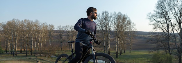 Radfahrer in Shorts und Trikot auf einem modernen Carbon-Hardtail-Bike mit einer Luftfedergabel, die auf einer Klippe vor dem Hintergrund eines frischen grünen Frühlingswaldes steht