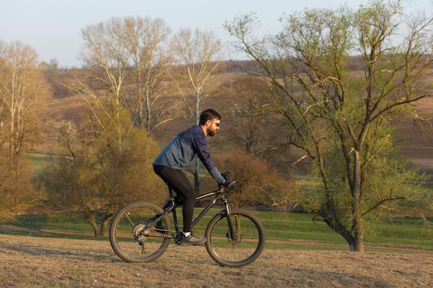 Radfahrer in Shorts und Trikot auf einem modernen Carbon-Hardtail-Bike mit einer Luftfedergabel, die auf einer Klippe vor dem Hintergrund eines frischen grünen Frühlingswaldes steht