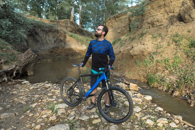 Radfahrer in Shorts und Trikot auf einem modernen Carbon-Hardtail-Bike mit einer Luftfedergabel, die auf einer Klippe vor dem Hintergrund eines frischen grünen Frühlingswaldes steht