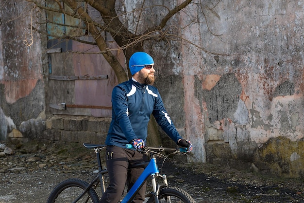 Radfahrer in Shorts und Trikot auf einem modernen Carbon-Hardtail-Bike mit einer Luftfedergabel, die auf einer Klippe vor dem Hintergrund eines frischen grünen Frühlingswaldes steht
