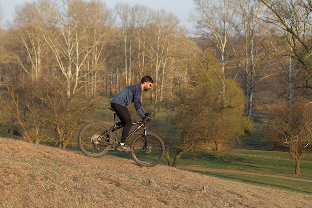 Radfahrer in Shorts und Trikot auf einem modernen Carbon-Hardtail-Bike mit einer Luftfedergabel, die auf einer Klippe vor dem Hintergrund eines frischen grünen Frühlingswaldes steht