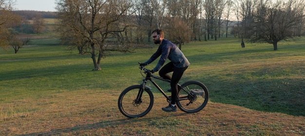 Radfahrer in Shorts und Trikot auf einem modernen Carbon-Hardtail-Bike mit einer Luftfedergabel, die auf einer Klippe vor dem Hintergrund eines frischen grünen Frühlingswaldes steht