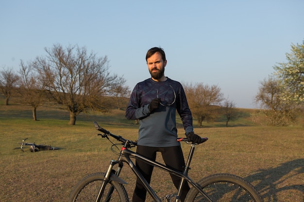 Radfahrer in Shorts und Trikot auf einem modernen Carbon-Hardtail-Bike mit einer Luftfedergabel, die auf einer Klippe vor dem Hintergrund eines frischen grünen Frühlingswaldes steht