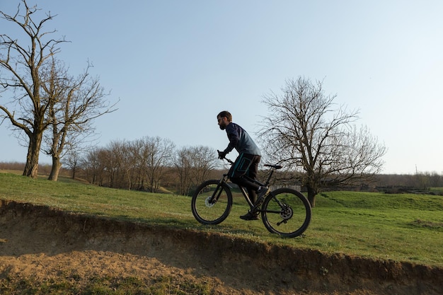 Radfahrer in Shorts und Trikot auf einem modernen Carbon-Hardtail-Fahrrad mit einer Luftfedergabel, die auf einer Klippe vor dem Hintergrund eines frischen grünen Frühlingswaldes steht