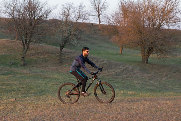Radfahrer in Shorts und Trikot auf einem modernen Carbon-Hardtail-Fahrrad mit einer Luftfedergabel, die auf einer Klippe vor dem Hintergrund eines frischen grünen Frühlingswaldes steht