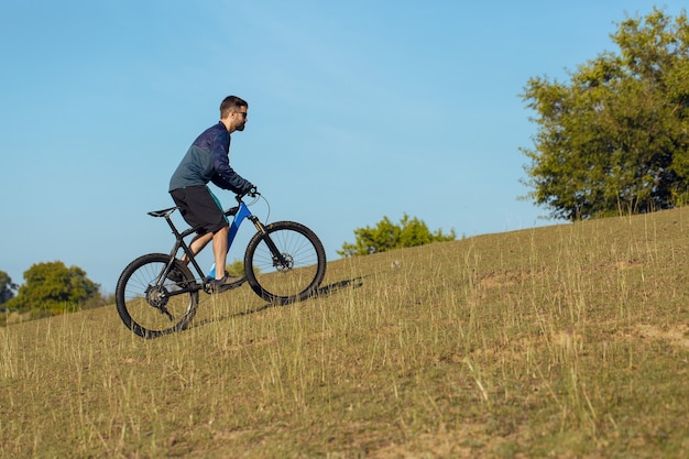 Radfahrer in Shorts und Trikot auf einem modernen Carbonrad mit Luftfedergabel auf einer Klippe stehend