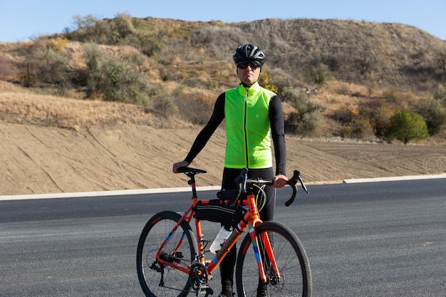 Radfahrer mit Fahrrad auf der Straße gegen den klaren Himmel Ein Mann in einem Outfit steht mit einem Fahrrad an einem sonnigen Herbsttag