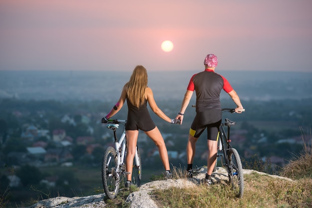 Radfahrer mit Mountainbikes auf einem Hügel bei Sonnenuntergang