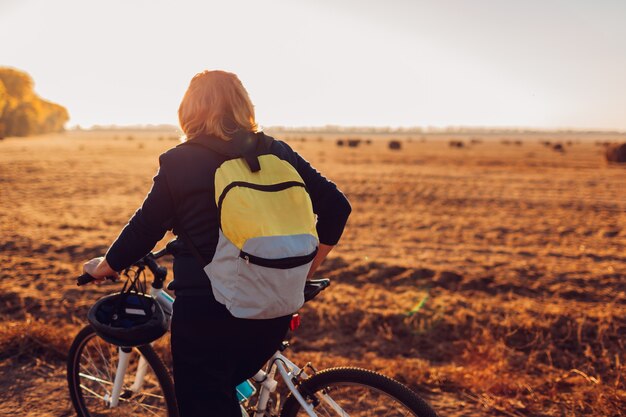 Radfahrerin mittleren Alters, die bei Sonnenuntergang im Herbstfeld reitet. Ältere Sportlerin, die die Aussicht bewundert.