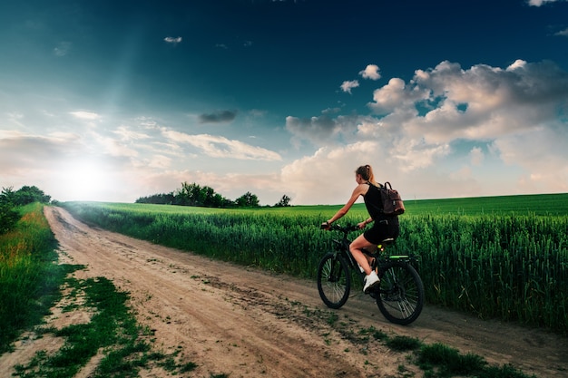 Radfahrermädchen am Sonnenuntergang auf dem Feld