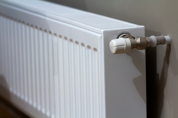 Radiador de aquecimento branco com válvula termostato na parede no interior de um apartamento após obras de renovação.