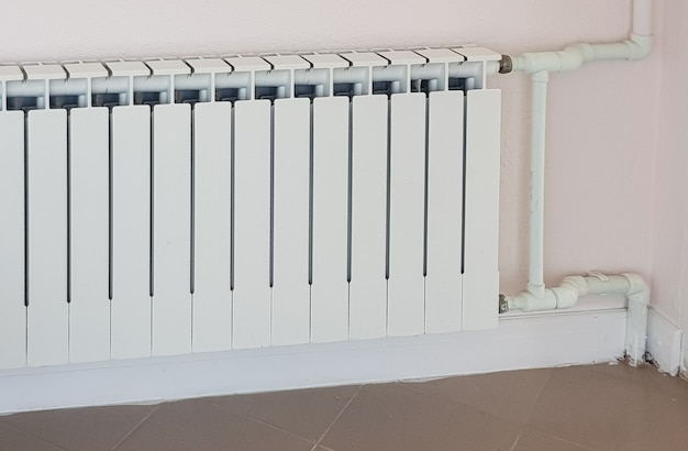 Radiador de aquecimento moderno de alumínio branco no fundo de uma parede em uma área residencial.