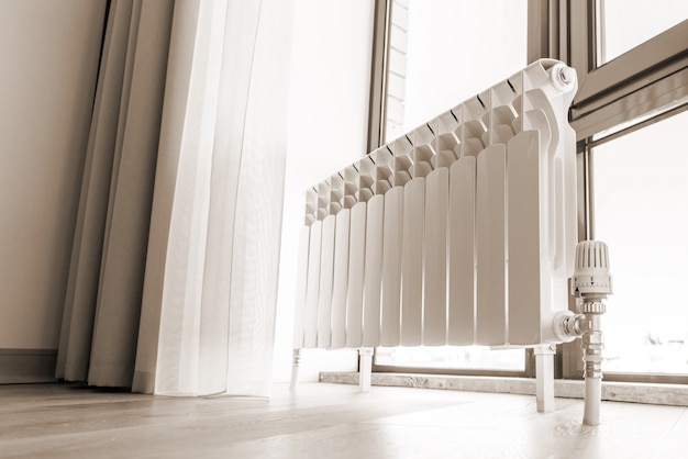 Foto radiador grande blanco cerca de la ventana en una habitación moderna, tonos sepia