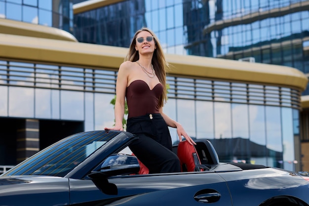 Foto en un radiante día de verano, el rostro de una mujer brilla con puro deleite mientras abraza la euforia de su nuevo auto convertible.