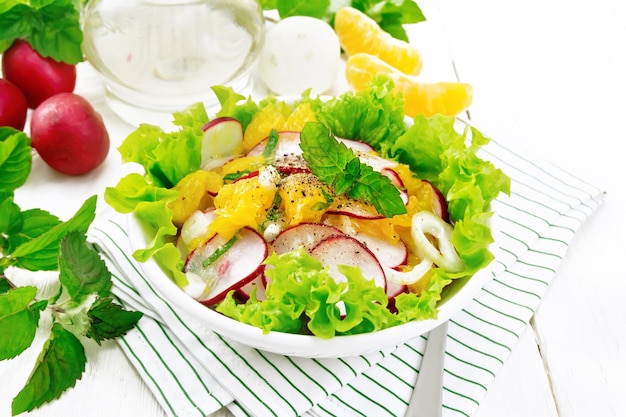 Radieschen-Zwiebel-Orangen-Salat mit Minze, Pflanzenöl und Gewürzen auf Salat in einem Teller auf einem Handtuch auf einem hellen Holzbrett